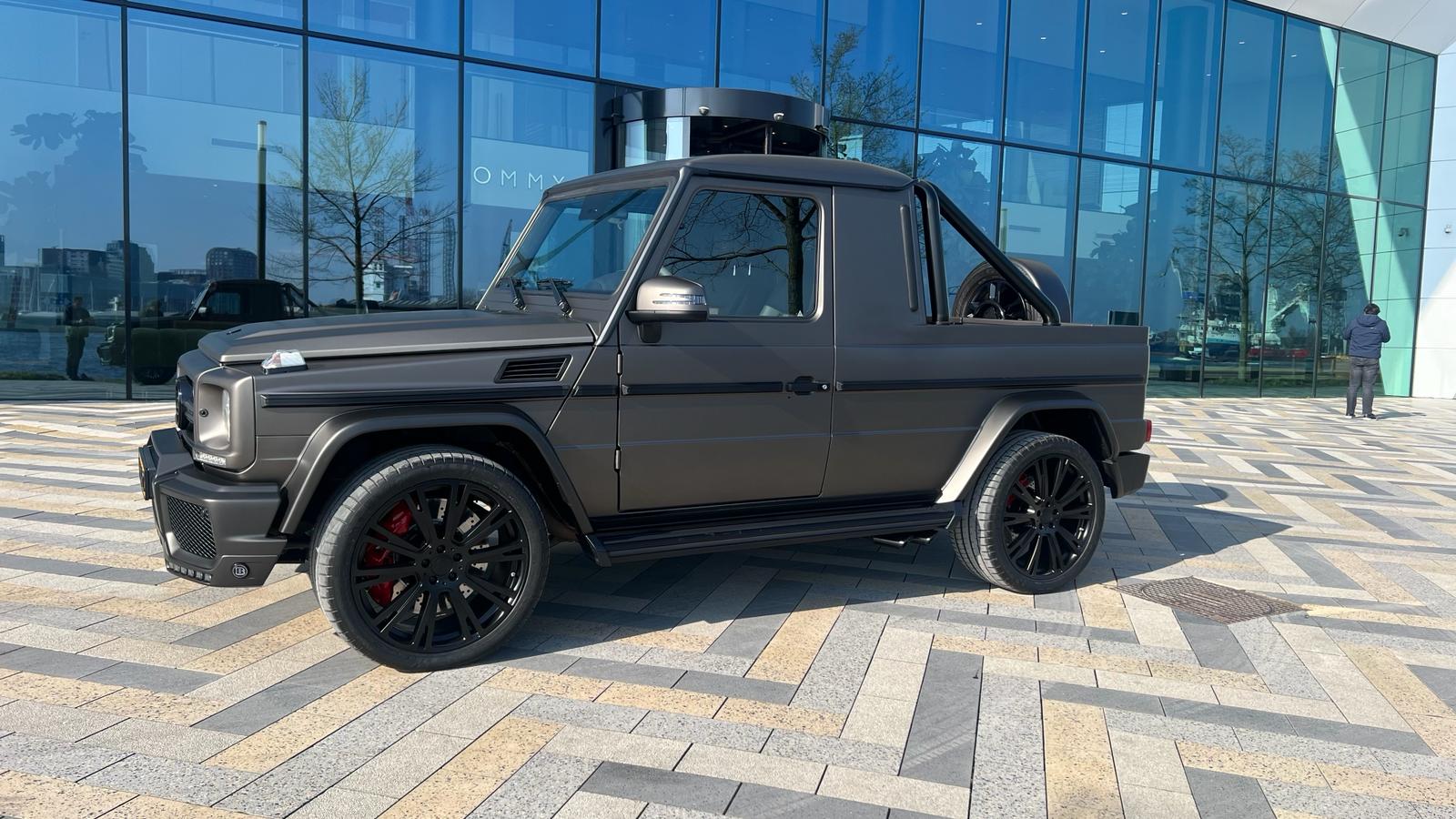 Mat grijze Mercedes G-klasse pick-up na afwerking, buiten voor een gebouw