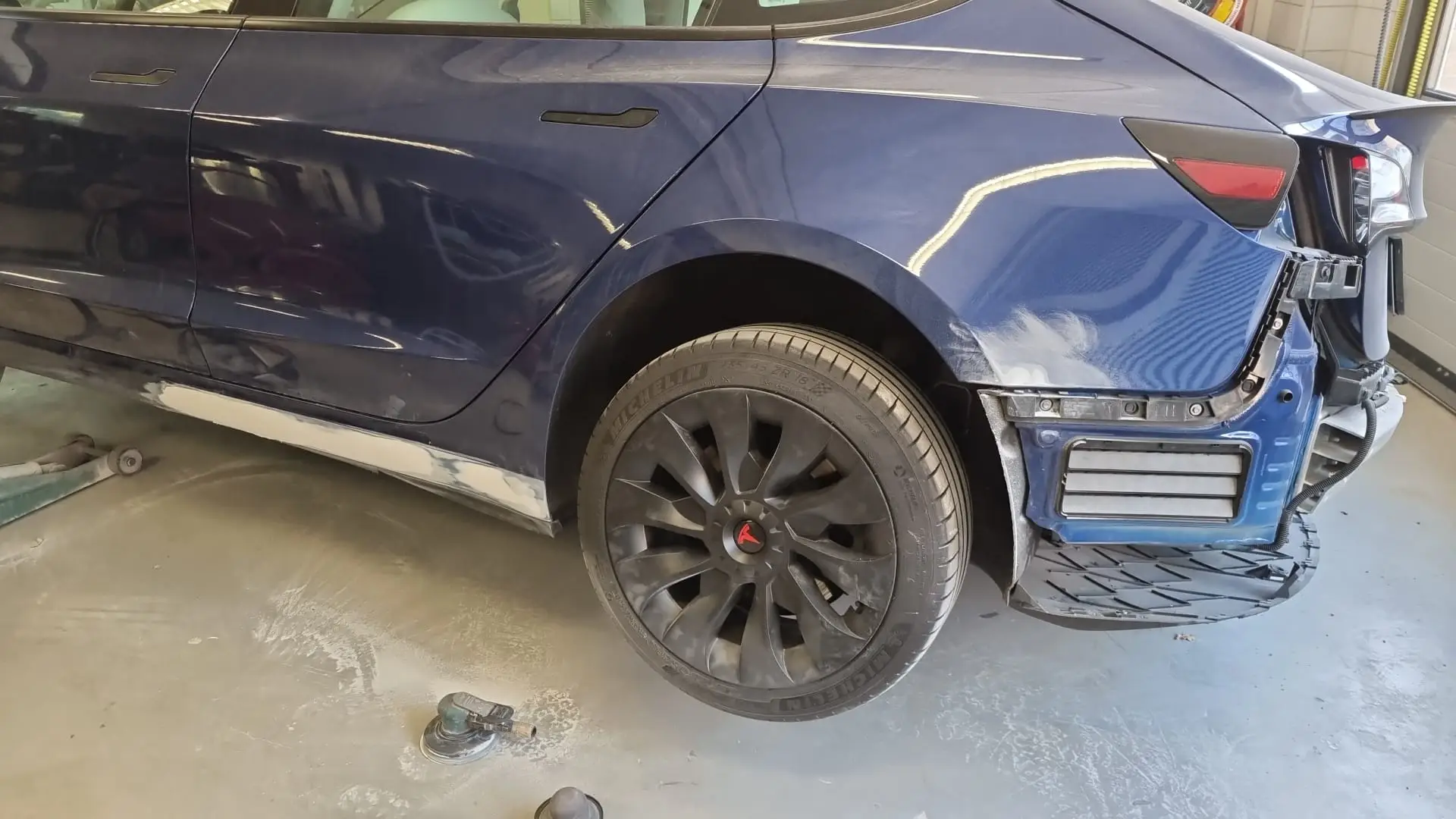 Donkerblauwe Tesla Model 3 met schade aan de achterzijde in de werkplaats