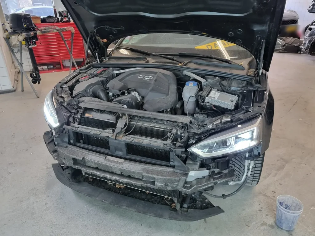 Audi A5 met geopende motorkap en gedemonteerde front tijdens schadeherstel in de werkplaats